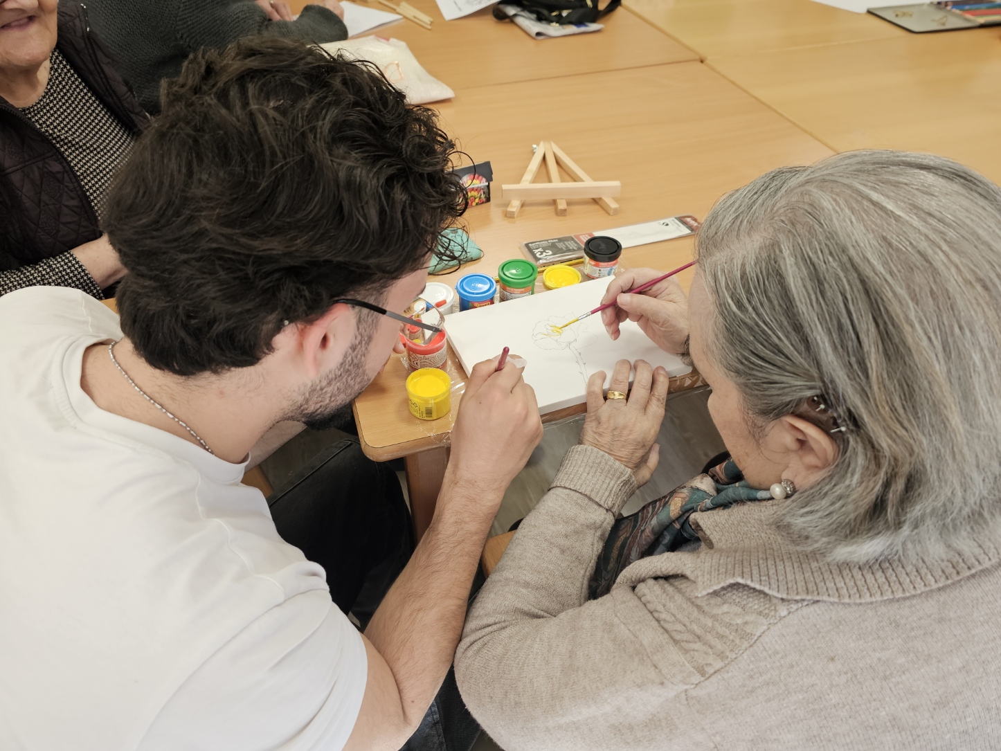 Estudiante y persona mayor pintando juntos con acuarelas