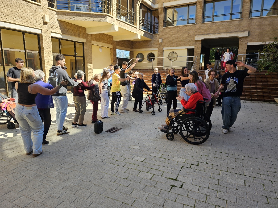 Mayores y estudiantes formando una rueda-cadeneta bailando juntos