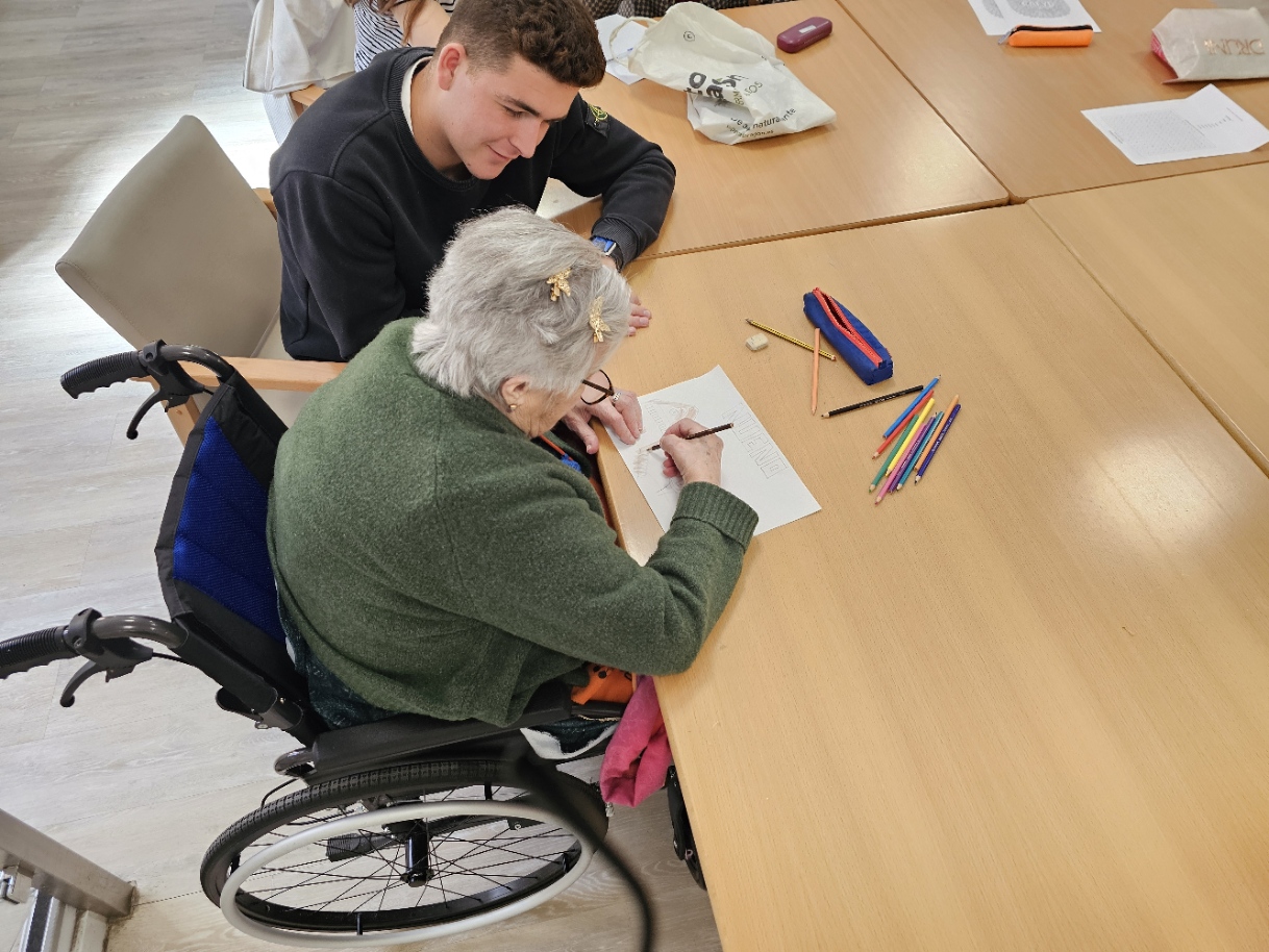 Tirso junto a una residente en silla de ruedas dibujando con pinturas de colores